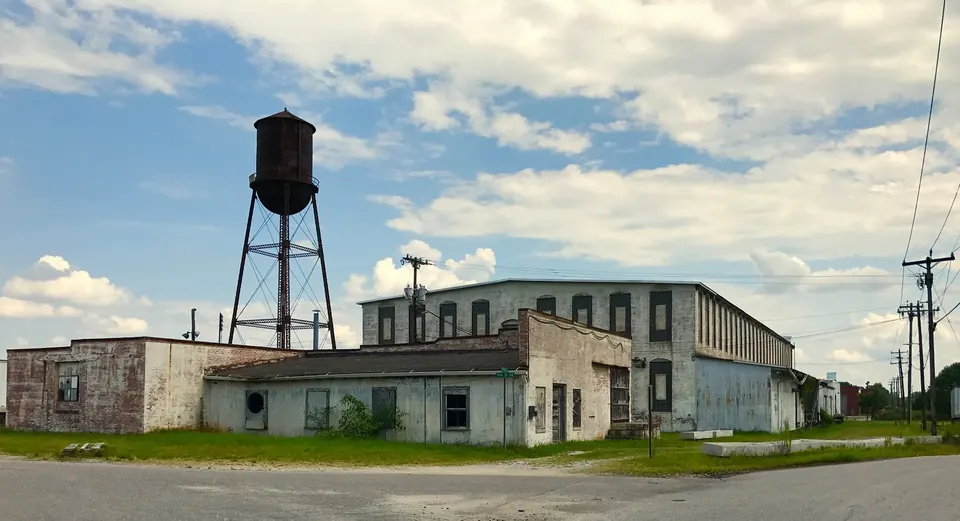 A long brick and block factory building in Conover with tall multi-pane windows and an old steel water tower beside it